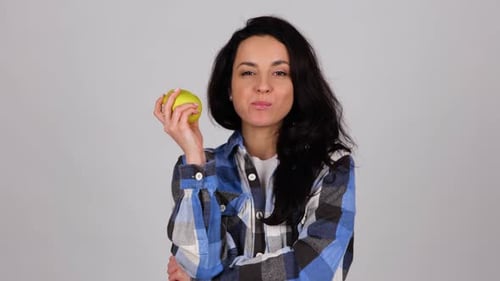 Happy Young Woman Biting a Juicy Yellow Apple While Posing in Studio on Grey Background Healthy