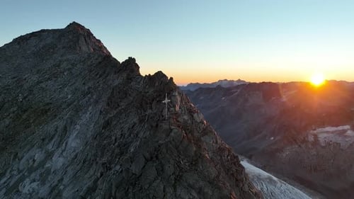 Mountain peak with a cross at sunrise. Drone footage in the Alps.