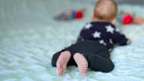Tiny toddler boy lying on belly and moving little bare feet. Close up.