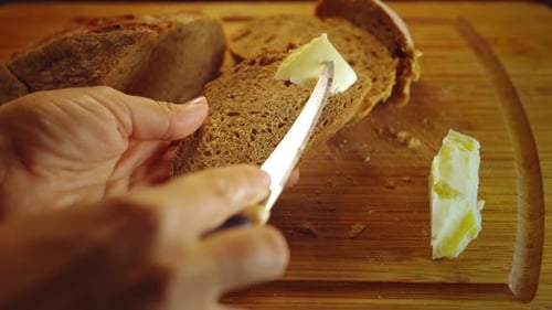 Close up of hand cut off piece of butter and spread on rye bread, top view of spreading butter