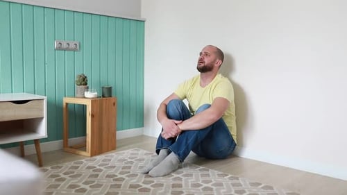 Man Sitting on Floor Leaning Against Wall in Bright Room During Daytime