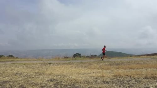 Cinematic aerial view of a sport man running on a countryside road