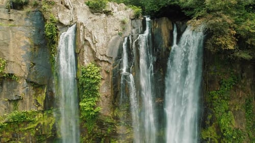 Tall waterfalls flowing down mossy cliffs surrounded by dense tropical forest