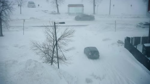 Car turns from building parking lot to road in heavy snow storm