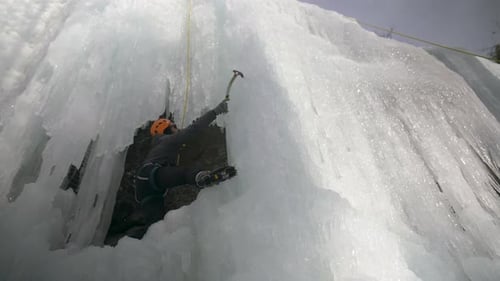 An adventurous man ice climbing up a sheer frozen rock face