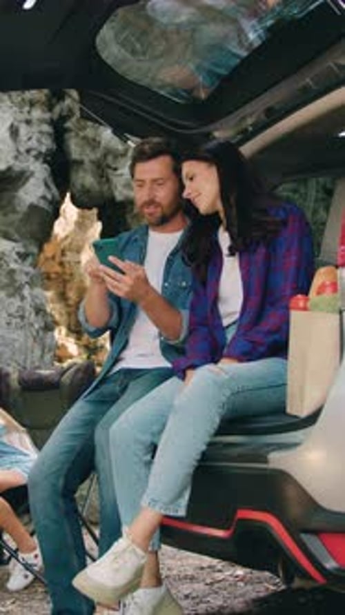 Couple Using Phone with Child near Car Trunk