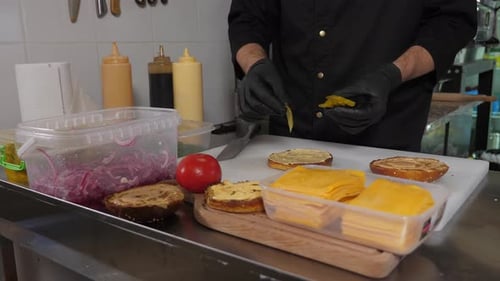 The Chef Preparing a Burger He Puts Various Ingredients on a Bun with Sauce