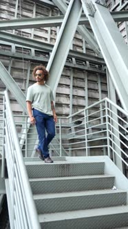 Young man with afro hair wearing sunglasses walking down the stairs in the city, urban fashion cool
