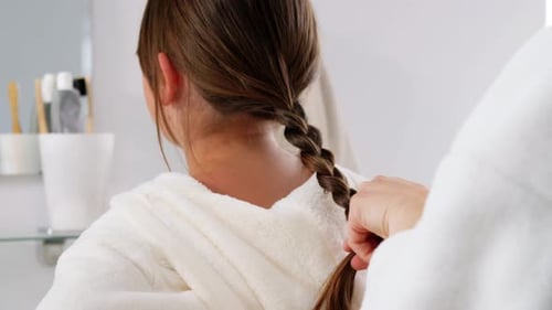 Young girl having her hair braided at home