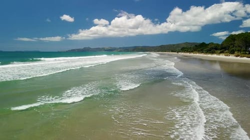 Aerial flight across the waves of secluded beach at high tide
