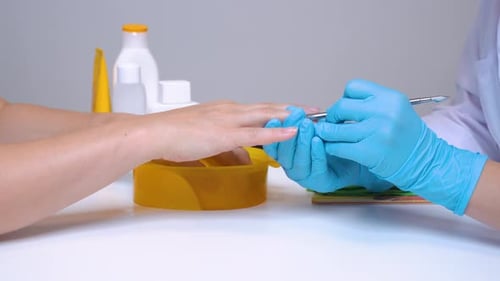 Close-up of the client’s hand and the nail master in processing nails in gloves will raise a cuticle