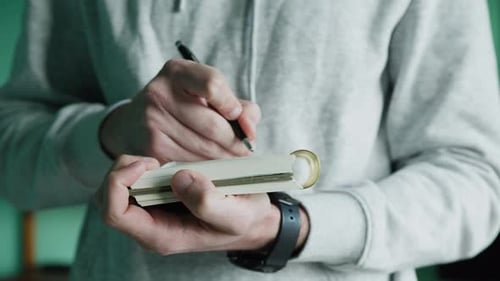 Close-up of Hands Writing in Small Notebook
