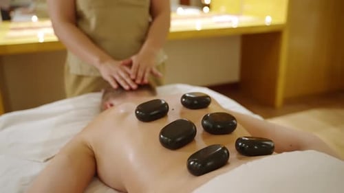 Female Spa Wellness Center Masseuse Puts Hot Stones to Client Back Woman Makes Massage Performs