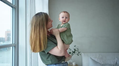 Loving Mother Holding Adorable Baby Indoors by Window