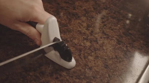 Une personne affûte un couteau dans la cuisine. - angle élevé
