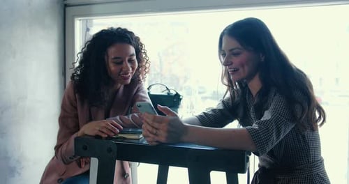 Two Happy Beautiful Multiethnic Female Friends Meeting at Coffee Shop Using Smartphone Social