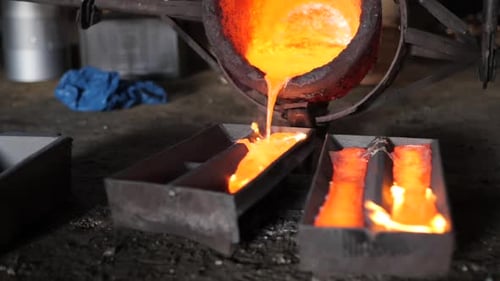 Industrial sized foundry bucket pouring flaming red metal into moulds with flames in a rustic