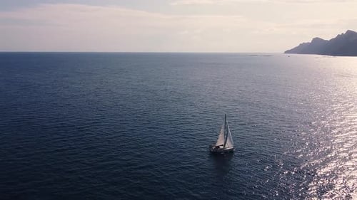 Sailboat sailing by coastline seashore against sunset and mountains. Sail boat in the south coast
