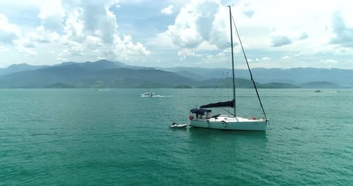 Aerial drone orbiting shot of moored sail boat in a turquoise calm ocean with people inside the boat