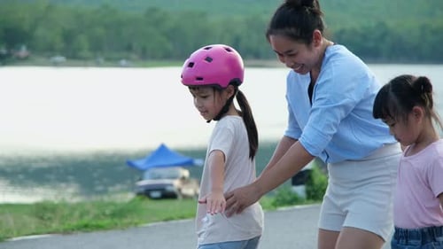 Mother teaching her daughter how to skateboard in the park. Child riding skate board.