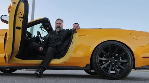 Mature Man Relaxing in Yellow Convertible A Relaxed Mature Man with a Beard Sitting in a Yellow