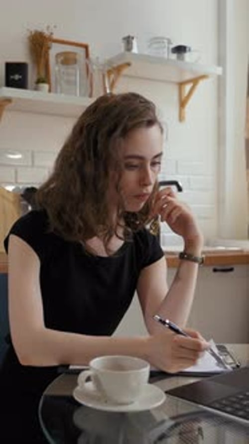 Vertical of Woman Makes Notes in Notepad Watching Lesson on Laptop