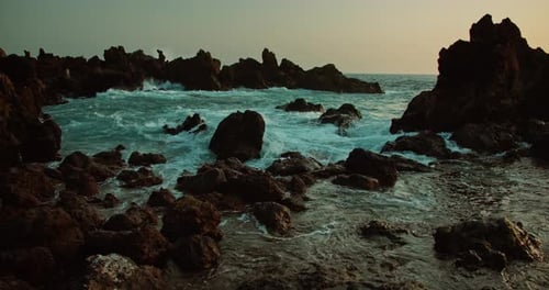 Plage volcanique rocheuse avec des vagues de l'océan éclaboussant des pierres de lave noires au crépuscule. Eau de mer moussante