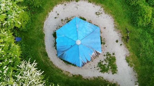 Rising over the blue roof of gazebo in the green nature. Blossoming trees grow around the lawn.