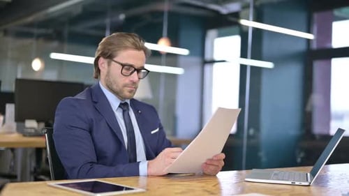 Man Reviews Documents at Office Desk