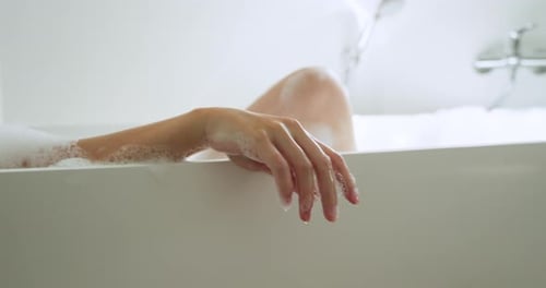 Mulher de spa reclinada em banho de espuma sobre toalha, movendo e estendendo o braço, formando gotículas para relaxar