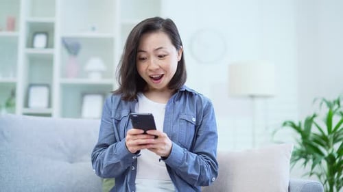 Woman Smiles, Celebrates While Using Smartphone Indoors