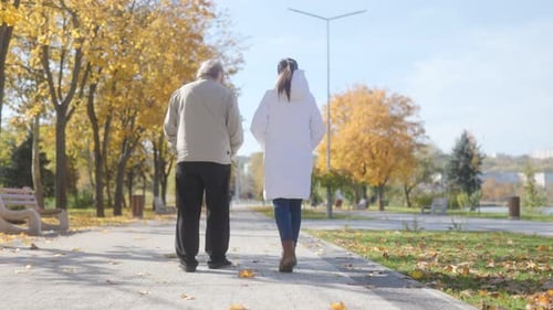 Senior Man and Female Caregiver Chat During Outdoor Walk