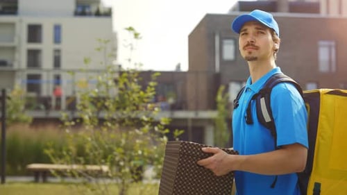 Side View of the Handsome Caucasian Male Courier Going Along the Building Holding the Paper Surprise