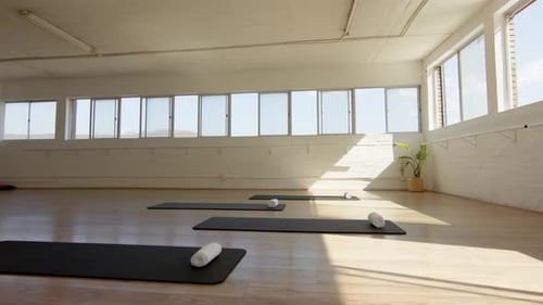 A serene yoga studio with black mats and white bolsters awaits practitioners, with copy space