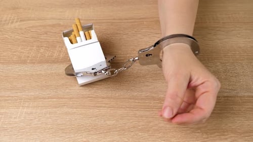 17c. A woman is handcuffed to a pack of cigarettes. Tobacco addiction concept. It's a shame to smoke
