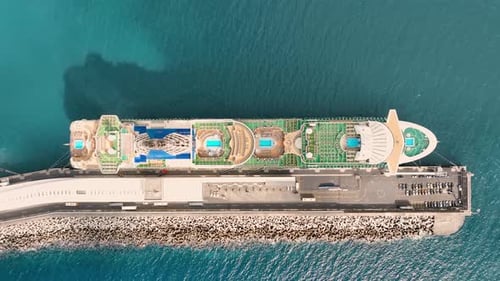 Cruise ship docked at port with pools and green spaces on deck