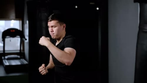 Boxeador entrenando en interiores Cámara lenta, golpes fuertes, brazos hinchados, un hombre feroz con una camisa negra, su