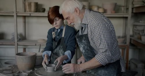 Elderly Man and Child Making Ceramic Bowl From Clay on Pottery Wheel in Arts Studio