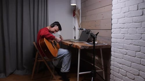 Man Plays Acoustic Guitar at Desk in Room