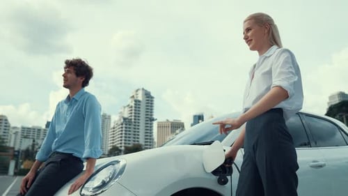 Progressive businessman and businesswoman use charging station for EV car.