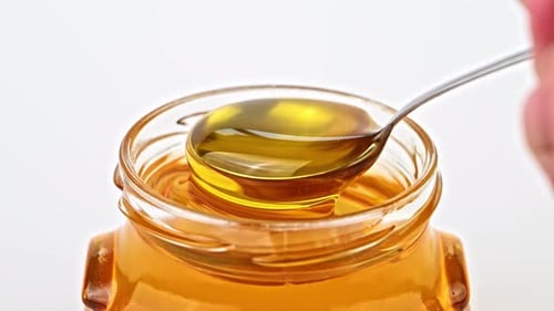 Golden Honey Being Poured into Jar with Spoon