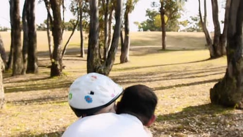 Father teaches son safety helmet use on park pathway steadicam shot