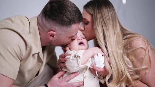 Caucasian parents kiss their adorable baby. Beautiful family of three portrait in studio. Close up.