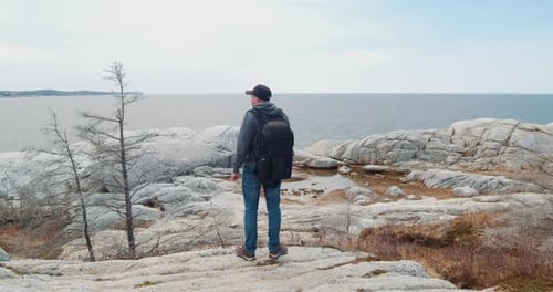Traveler with a Backpack Standing on a Rocky Hill Overlooking the Ocean