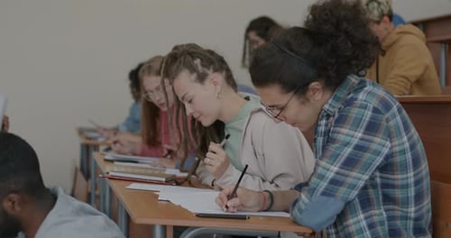Gruppe junger Leute, die einen Test schreiben und lernen, während der Lehrer an Schreibtischen im Klassenzimmer sitzt