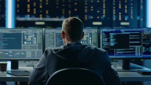 Man Works at Multiple Computer Monitors Late at Night