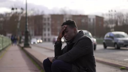 Anxious black man sitting on sidewalk feeling worried