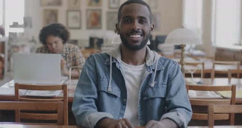 Slow Motion Portrait of Cheerful African American Man Student Sitting at Desk in Library Smiling