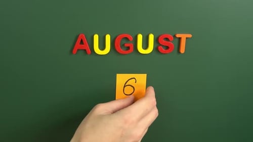Hand sticking a sticker 6 August calendar day on school board. 6 date of august. Sixth day