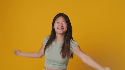 Smiling young woman dancing isolated over yellow background in studio